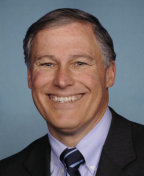 close up portrait of jay inslee grinning against blue background