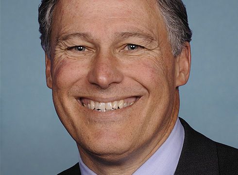 close up portrait of jay inslee grinning against blue background