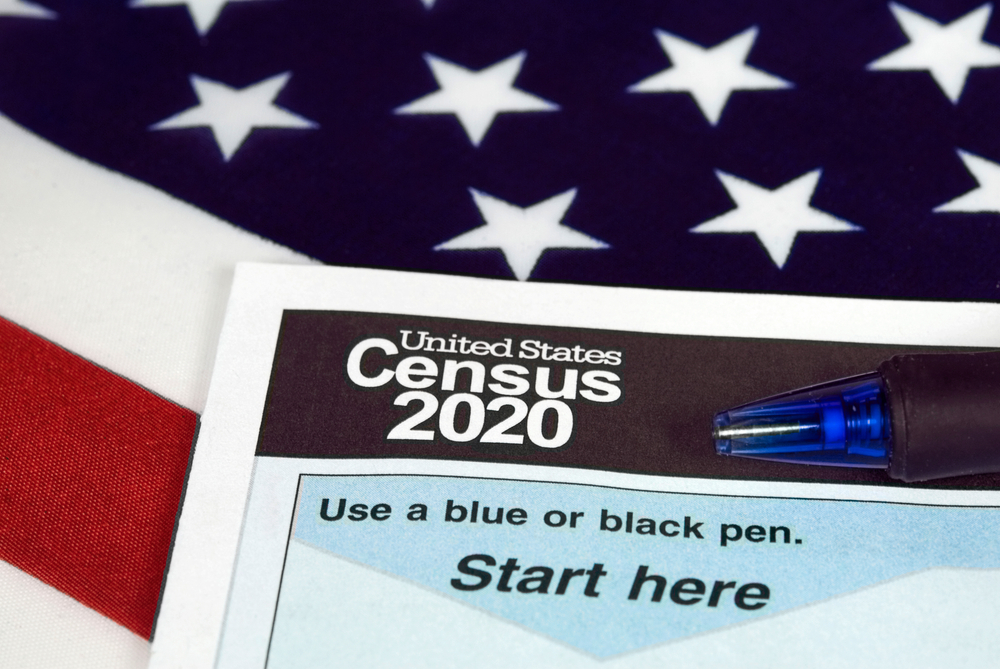 census form on top of american flag. form says 'united states census 2020. use a blue or black pen. start here.'