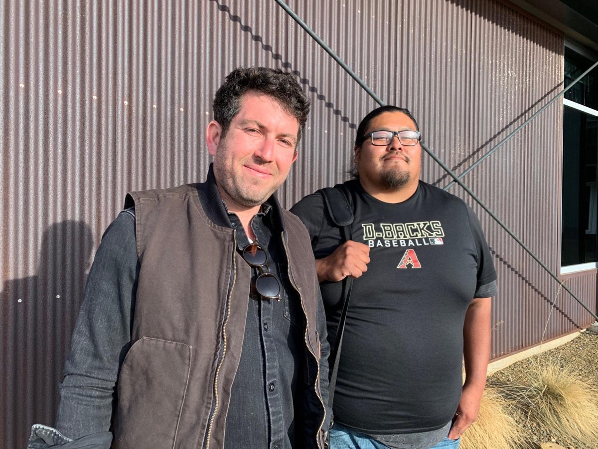 two men stand in front of a shed like building