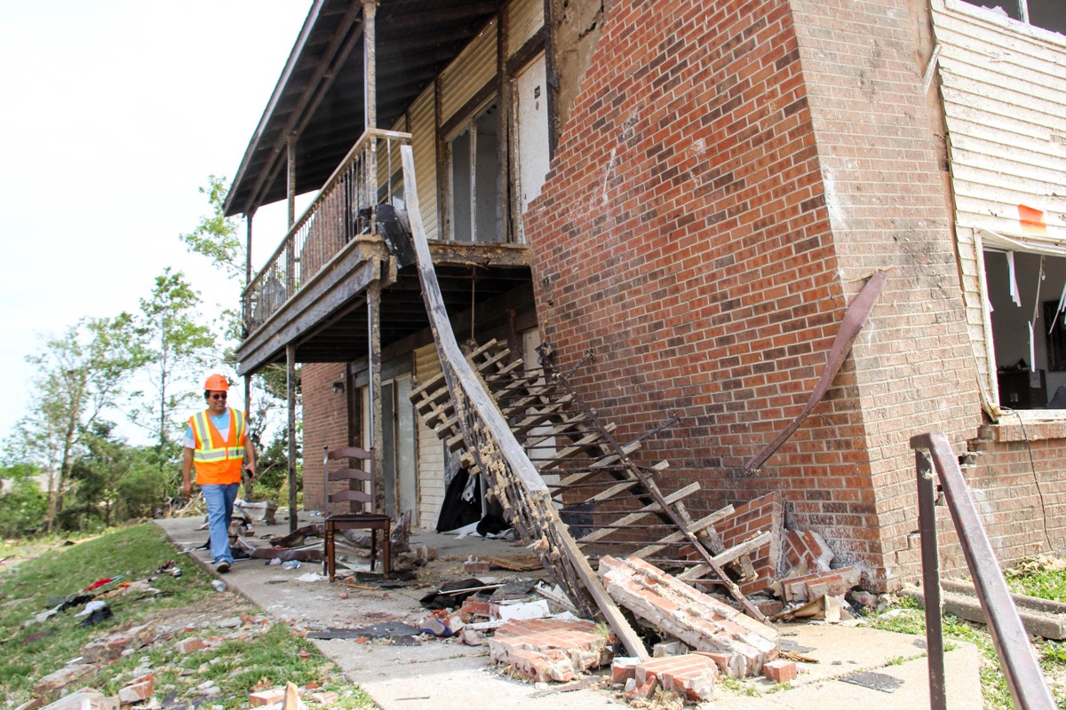 An engineer walks alongside a building where the brick siding has separated from the wall. a staircase has also fallen