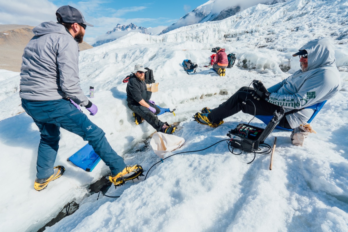 three research scientists gather together on a glacier collecting data 