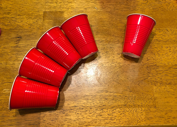 four cups taped together, with the bottom edges touching together so that it looks like the row of cups is creating an arched bridge