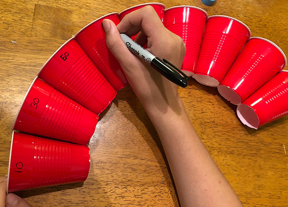 eight cups are taped together, creating a nice curve. a person begins to write in sharpie different numbers on the cups