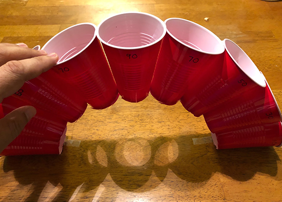 the arch of cups are propped upward on a table to create a bridge like structure