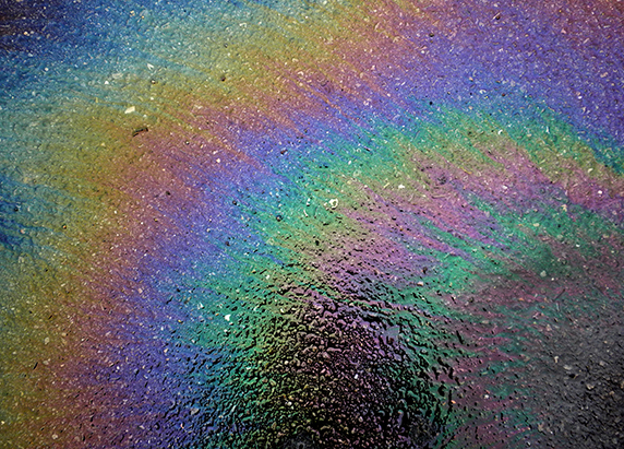 a close up of an oil slick on pavement. a rainbow of color fans outward on the pavement