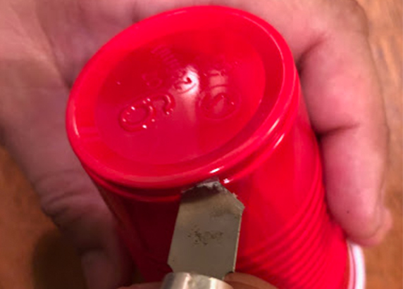 a hand holds a red solo cup, bottom up and pierces the bottom with an exacto knife