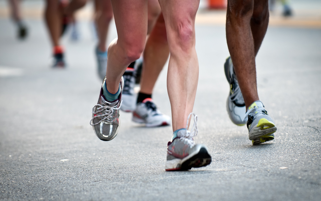 up close image of multiple pairs of legs of men and women and white people and people of color running down a track