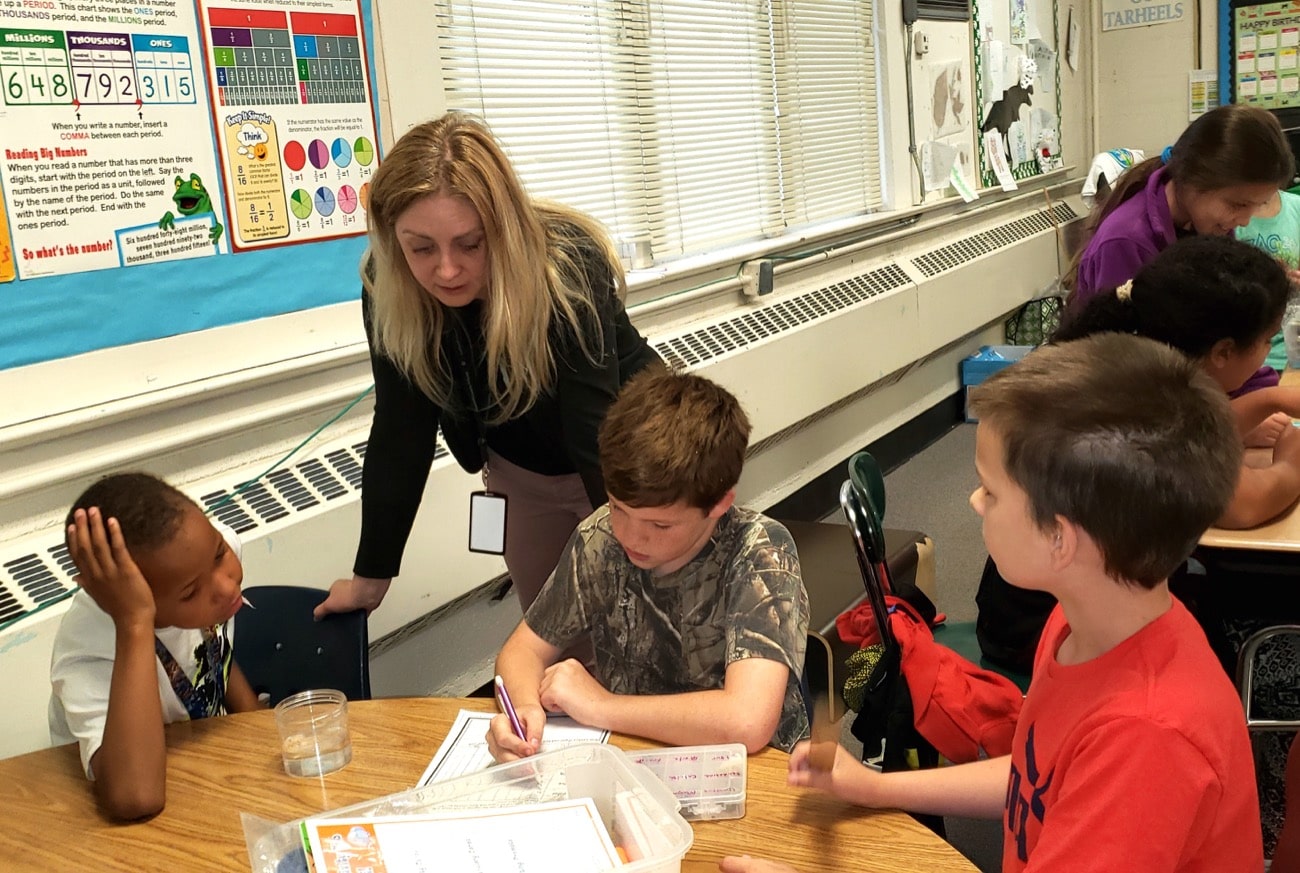 a woman in a classroom stands over a table with three children