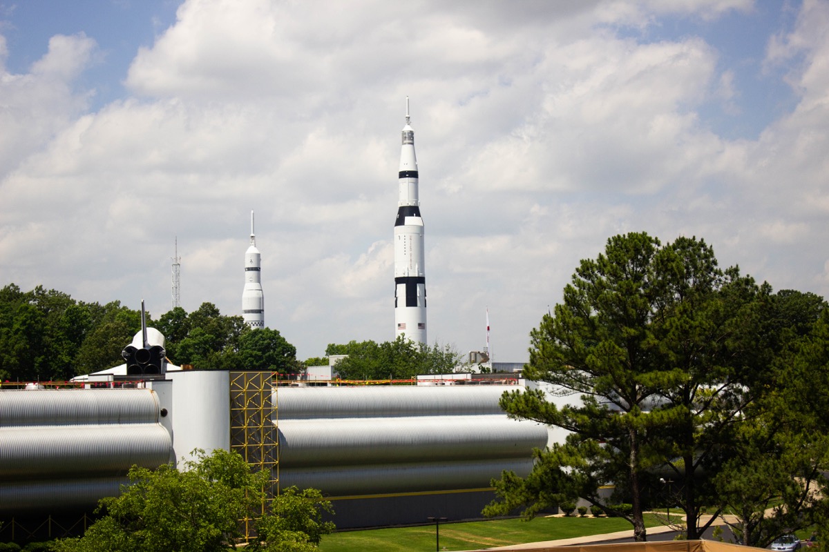 a rocket stands in the distance on a bright day. there are trees and other types of smaller rockets nearby