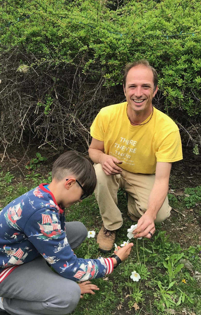 a man kneeling in the grass holding a flower, along with a kid next to him