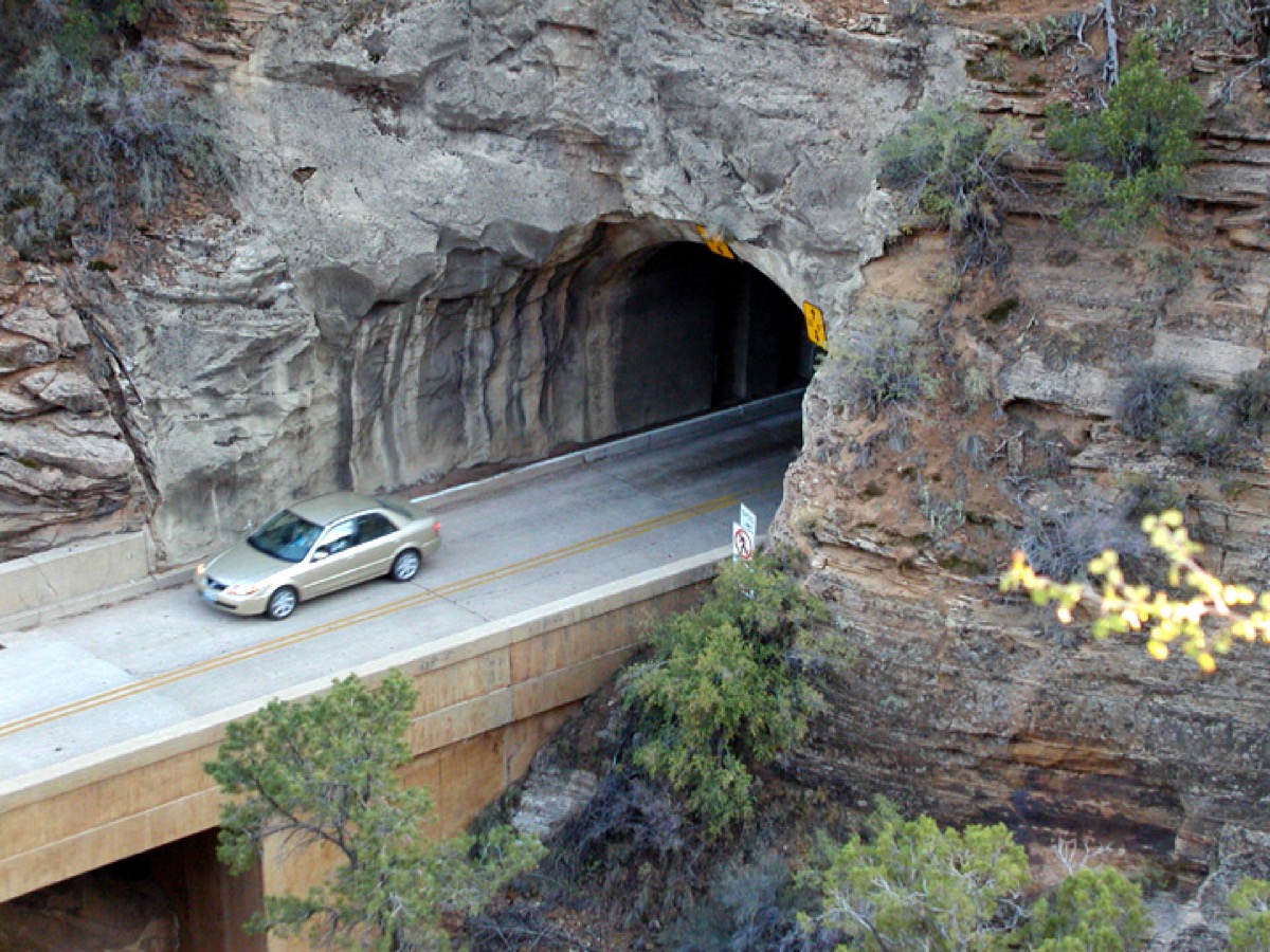 a car on a bridge, about to enter a tunnel on the side of the mountain