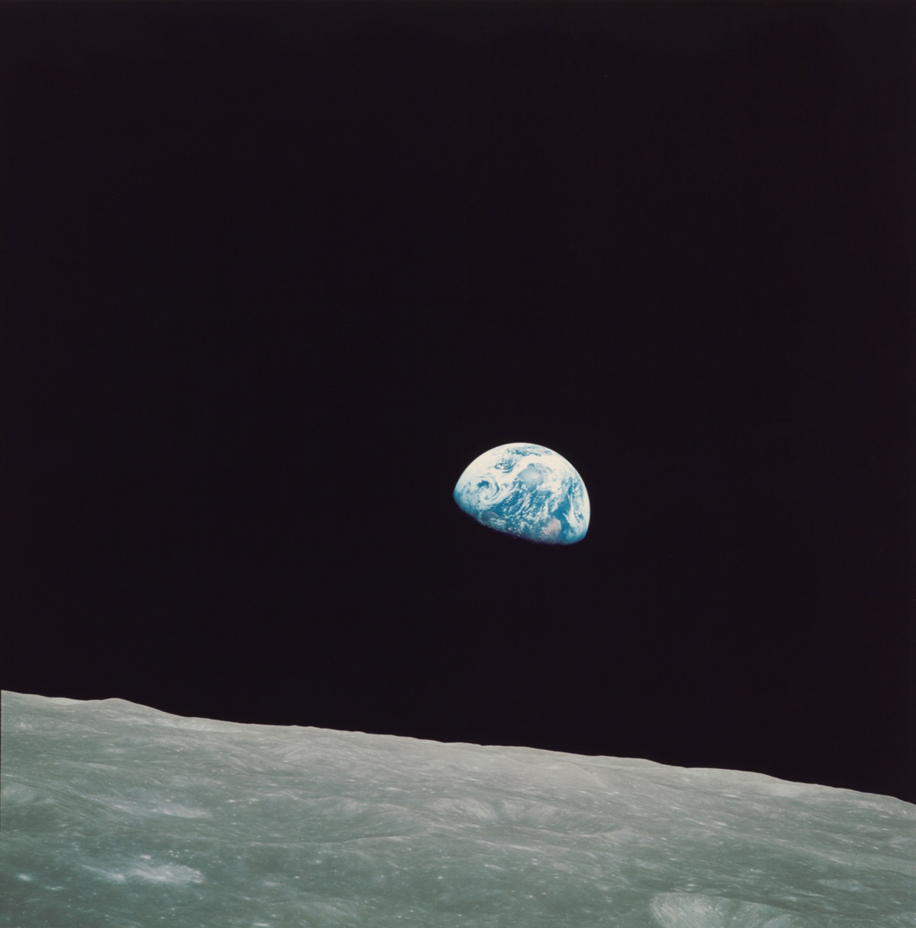 the curve of the moon in the foreground with the earth, half in shadow, sitting in the blackness of space