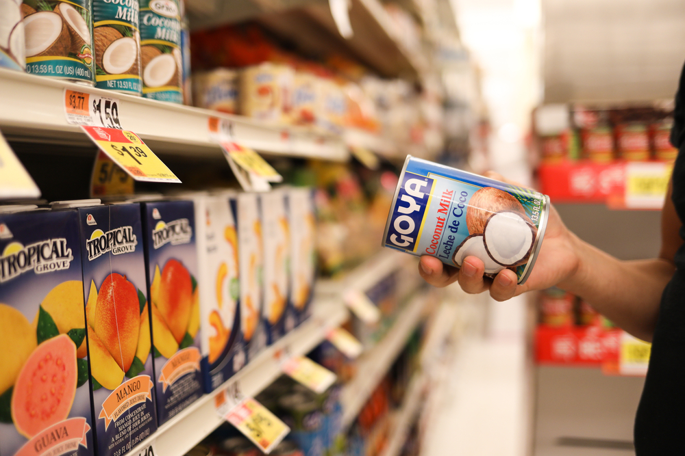 a person at the grocery store holds a can of coconut milk