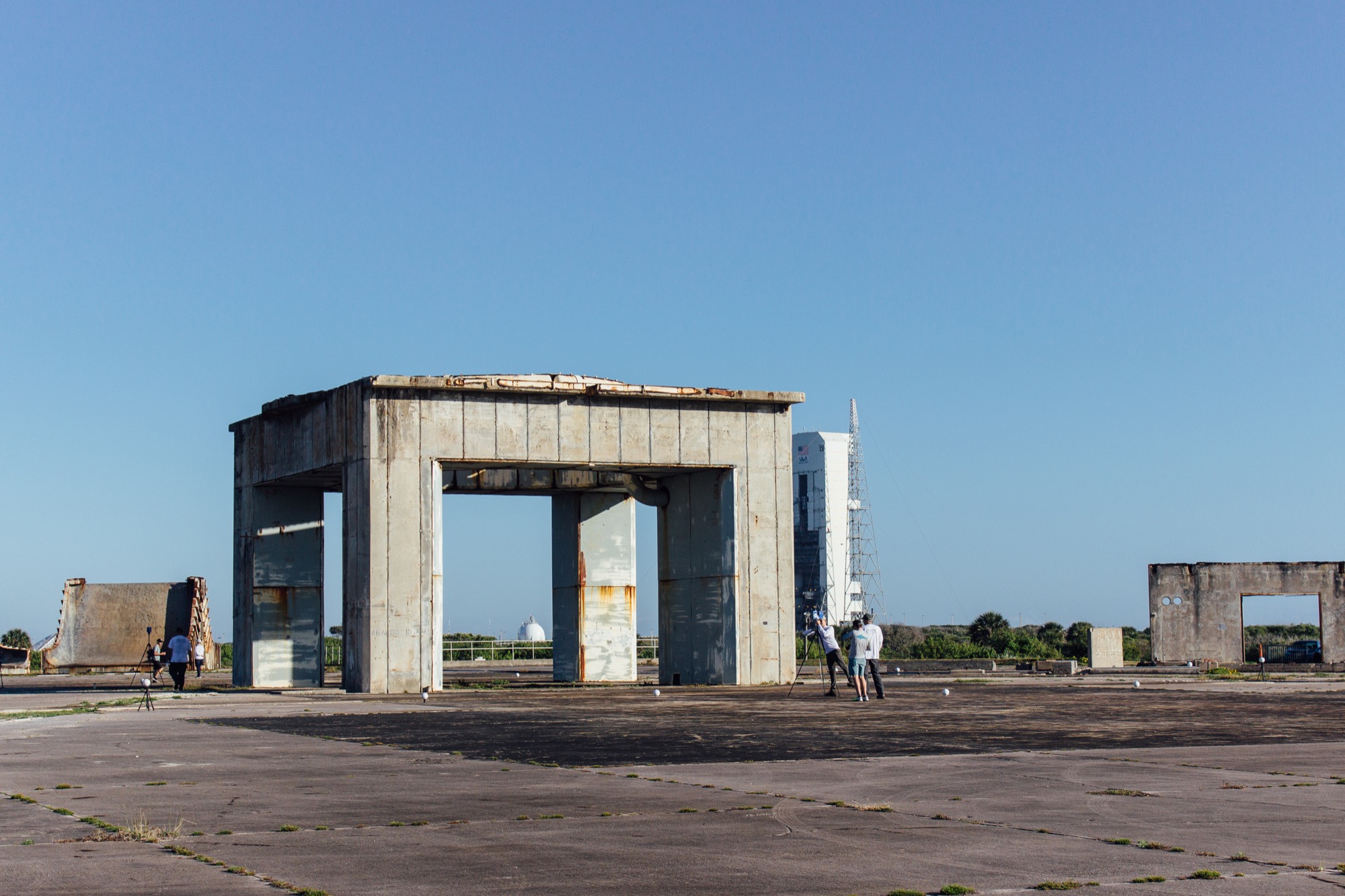 A square concrete structure with four legs and a large ramp, with a modern launch tower in the distance