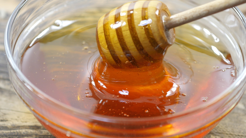 a wooden spoon dips into a bowl of golden honey