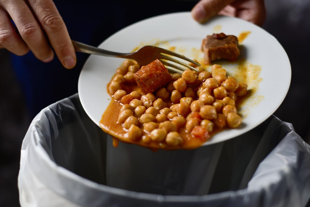 someone scraping beans and meat from a plate into a trash can