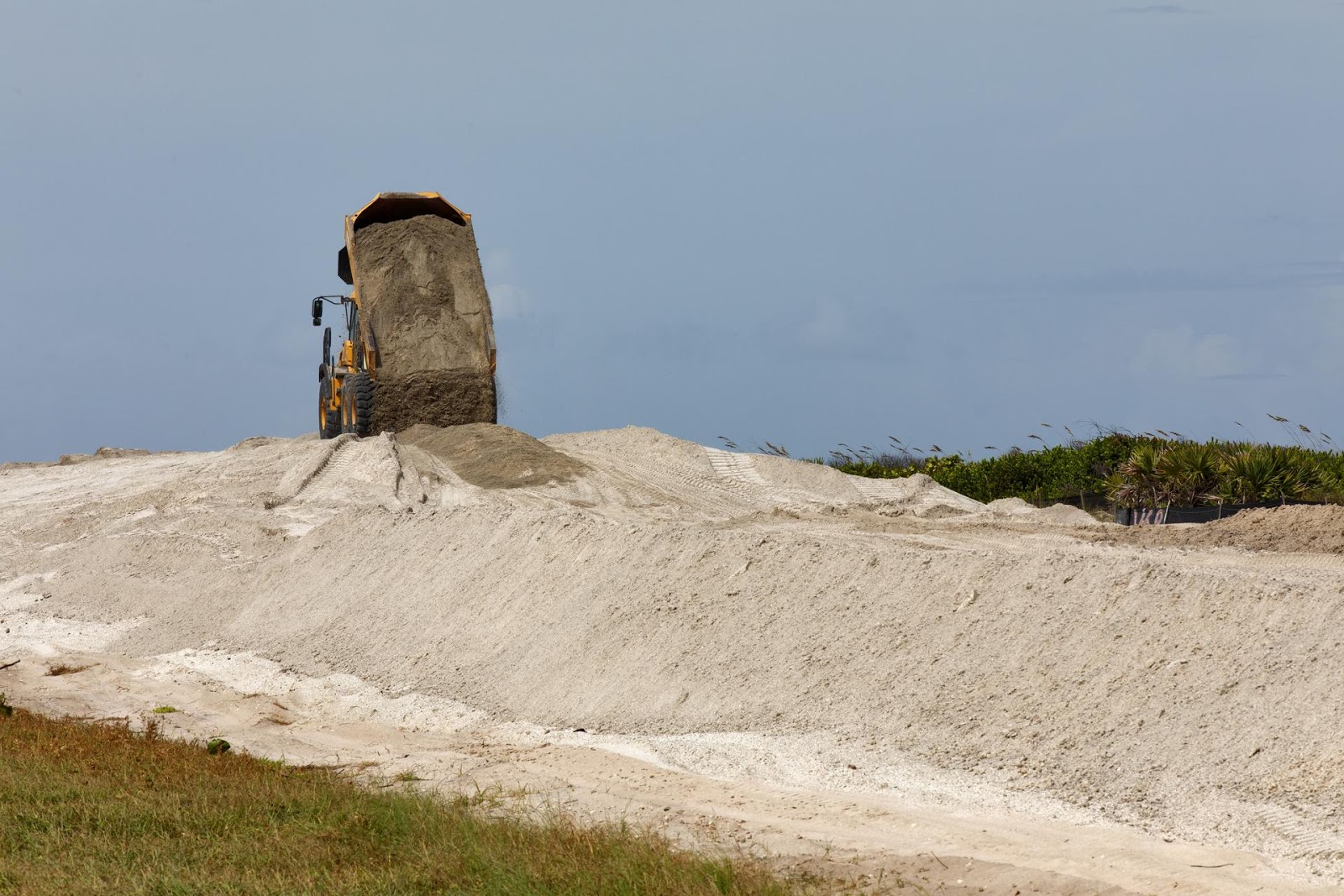 a dump truck on top of a large sand dune dumping more sand onto it