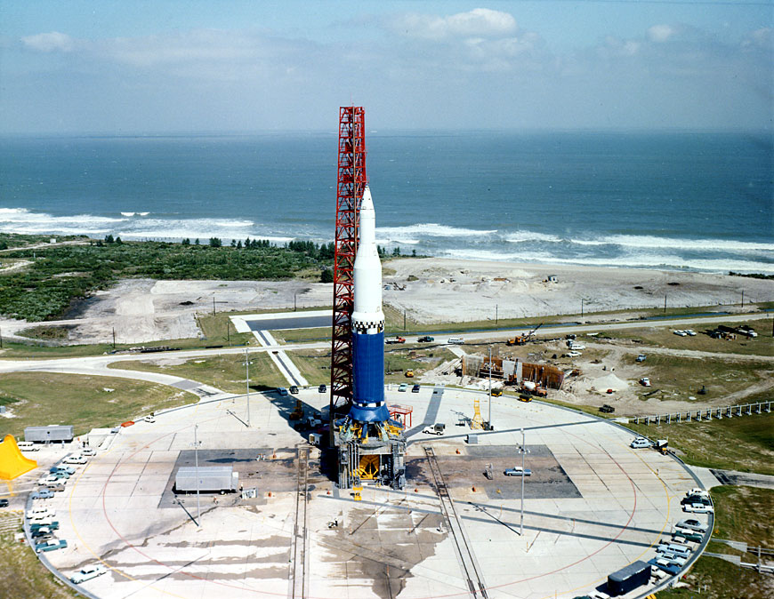 a ariel photo looking at a large rocket with a tower next to it with the ocean in the background