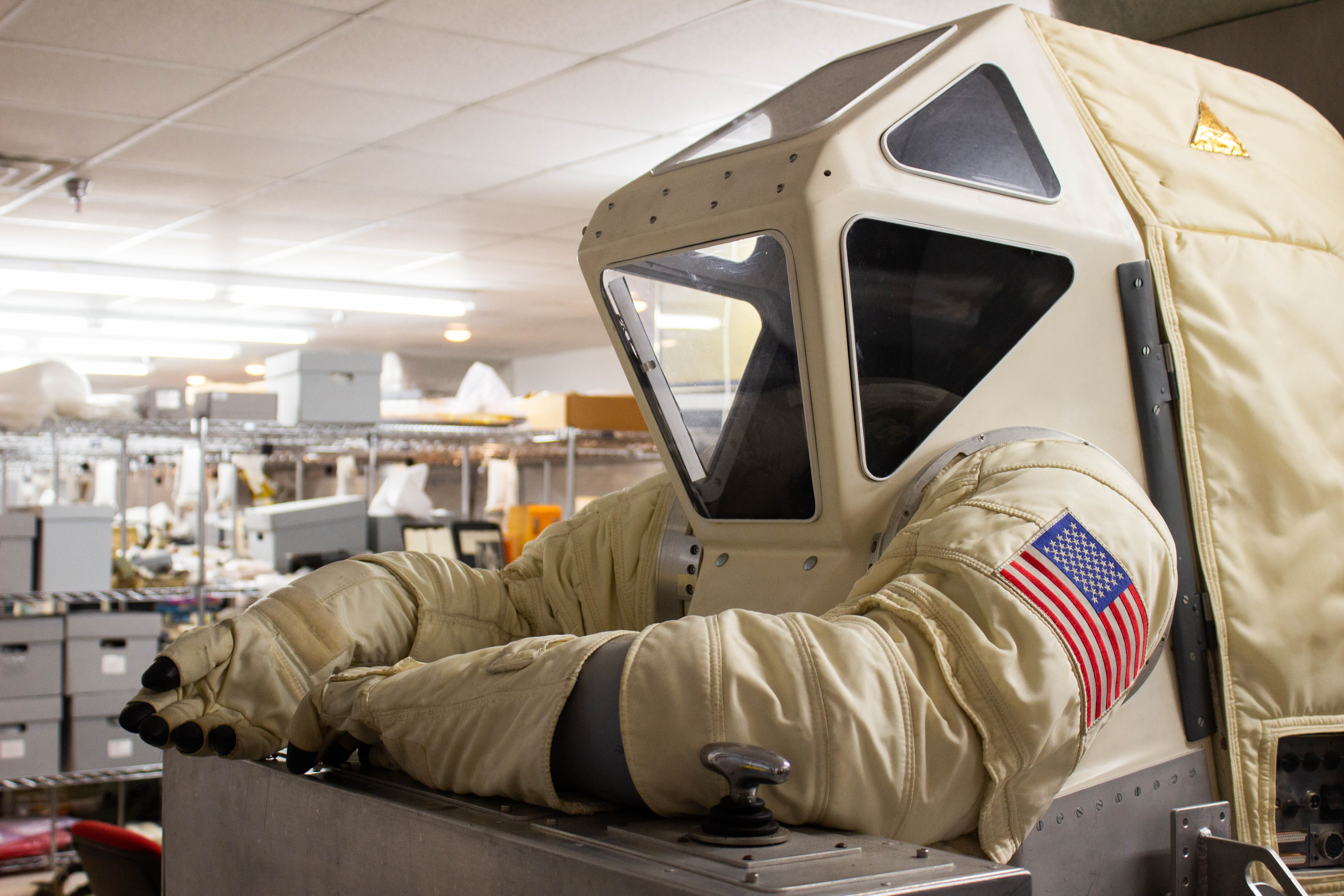 off-white empty spacesuit propped up with storage boxes in the background