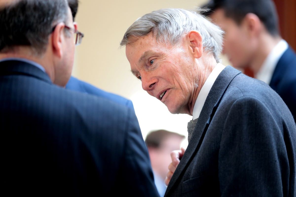 an older white man in a black suit talking to another man in glasses