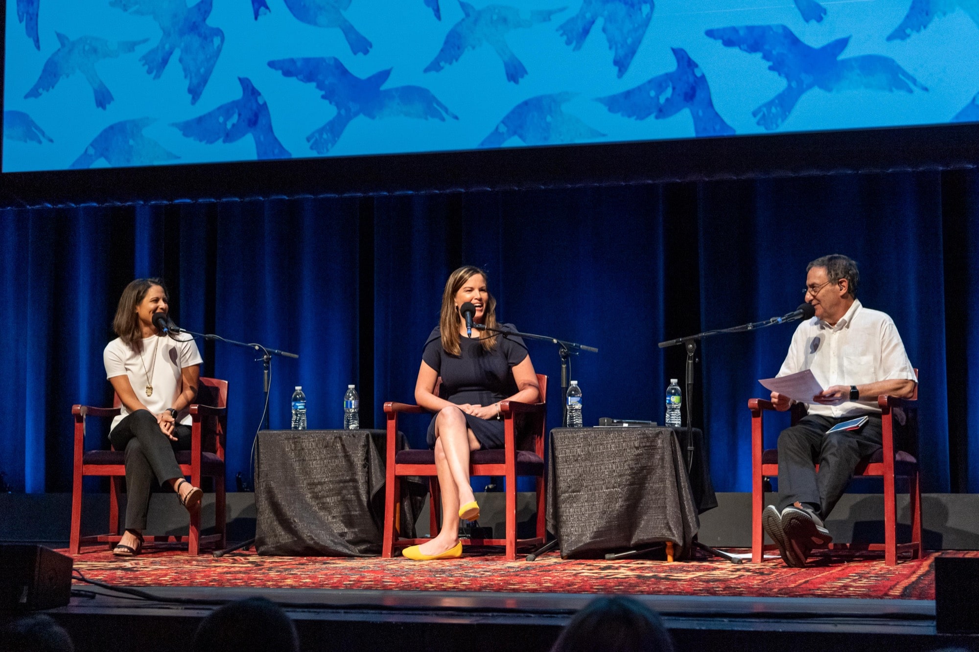 two women and one man sit on chairs on a stage, each with microphones