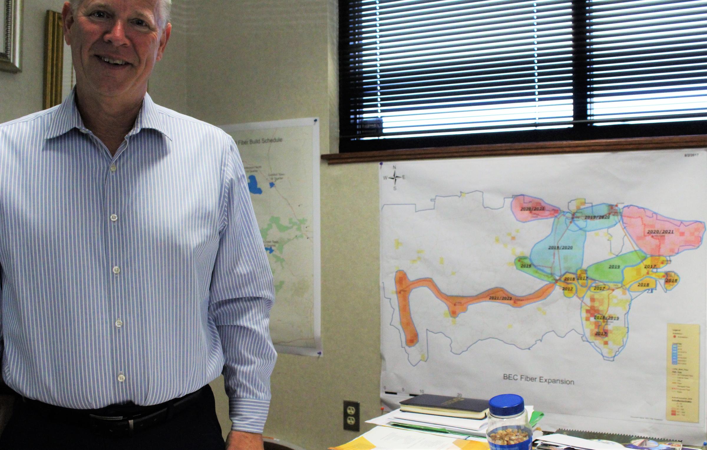 man in suit stands in front of map with several colors, showing how the company plans to expand in the area