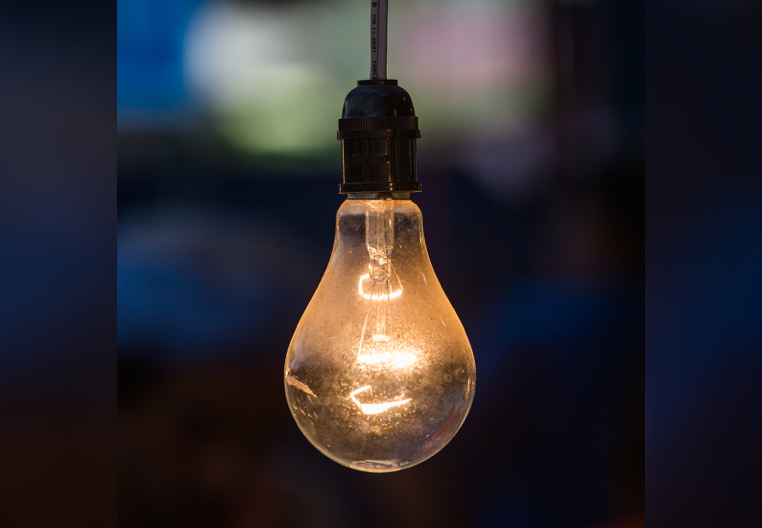 an old, glowing lightbulb hanging against a darkly colorful background