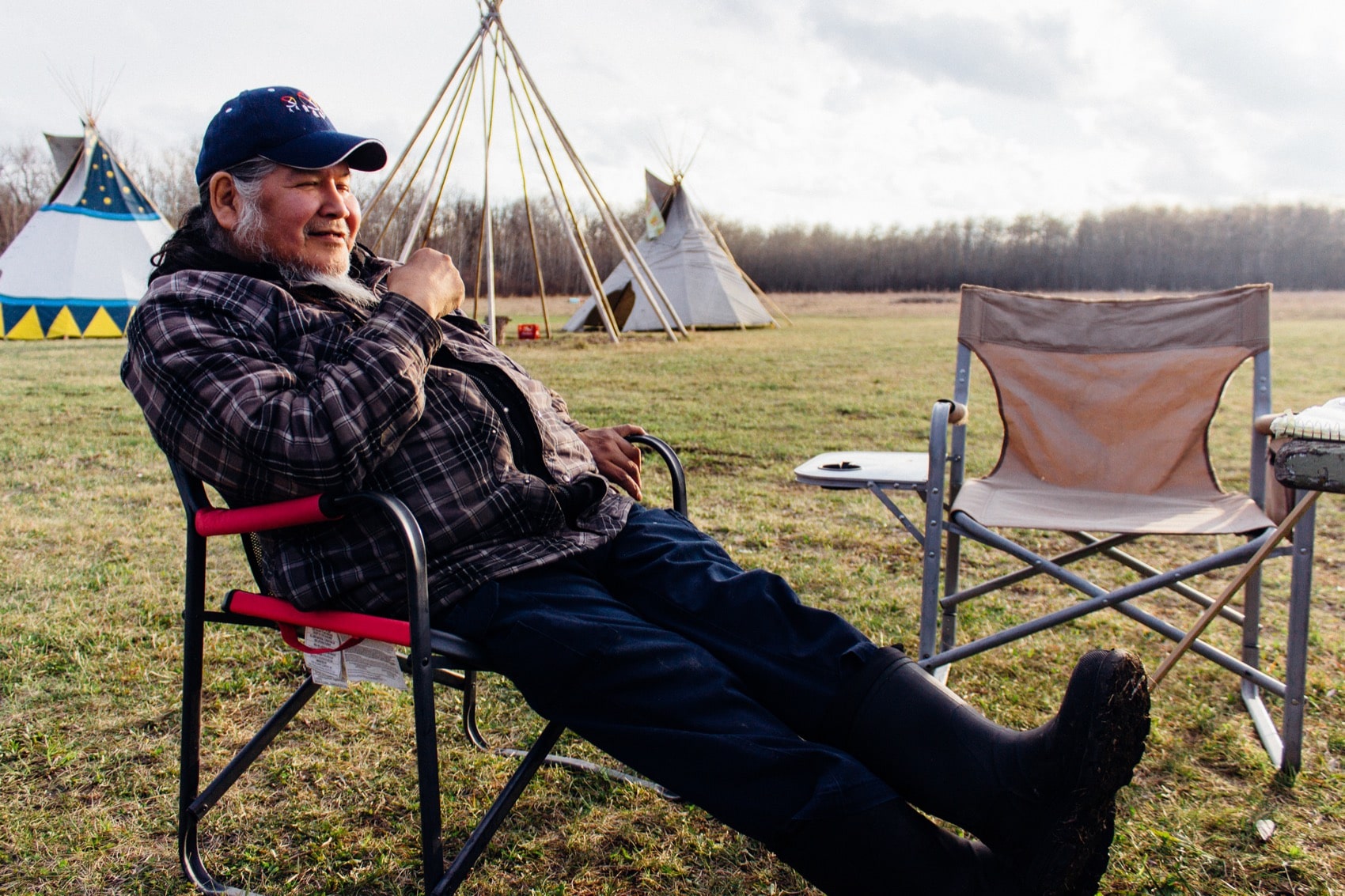 a man sits on a lawn chair in a field with tipis in the background