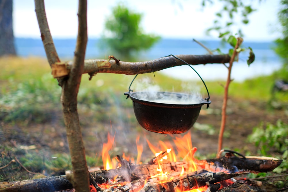 a pot hanging over a fire outside, suspended by a stick contraption