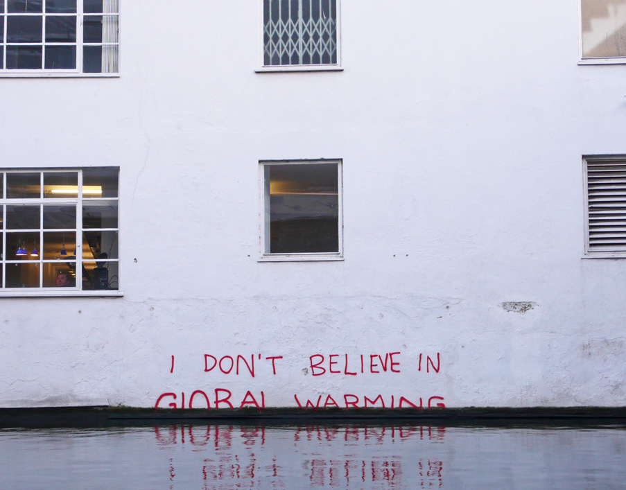 water reaching up high to the edge of a building. right at the edge of the building where the water meets the building are the words in red graffiti "i don't believe in global warming." the words appear to be slipping beneath the water line