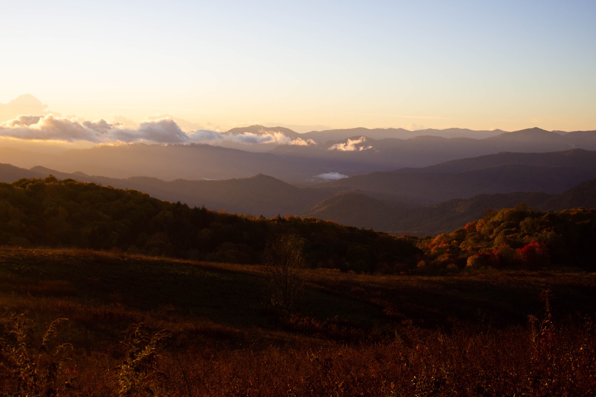 sun rise over folds of mountains, making them glow red with the autumn leaves