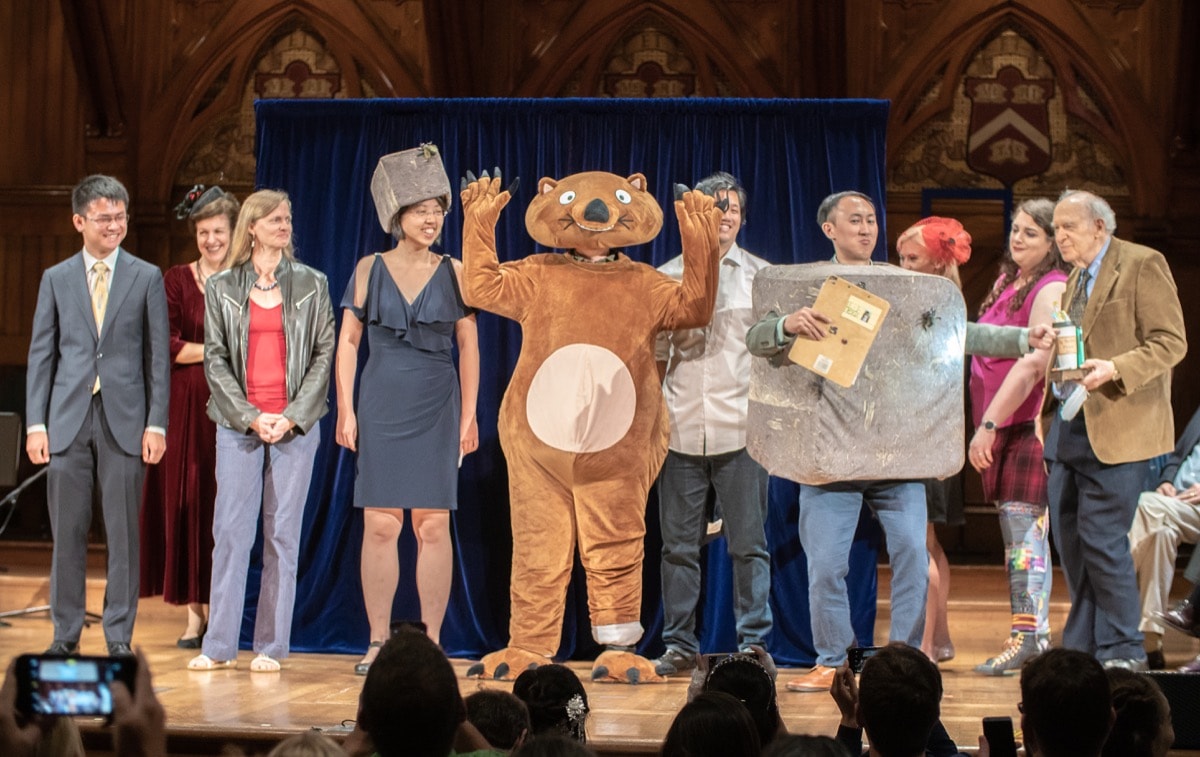 a group of scientists on stage, one is dressed as a wombat and another is dressed up as a cubed wombat poop