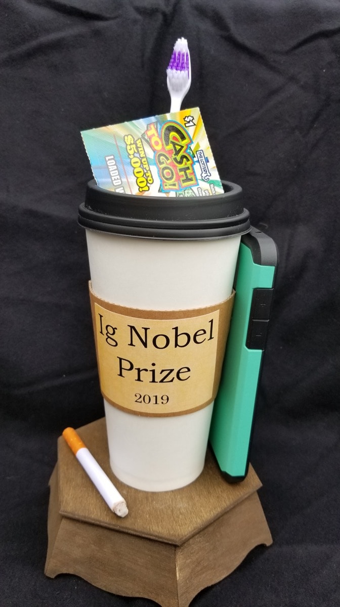 a coffee mug with a tooth brush, a cellphone case, a lotto ticket, and a used cigarette constructed as a trophy