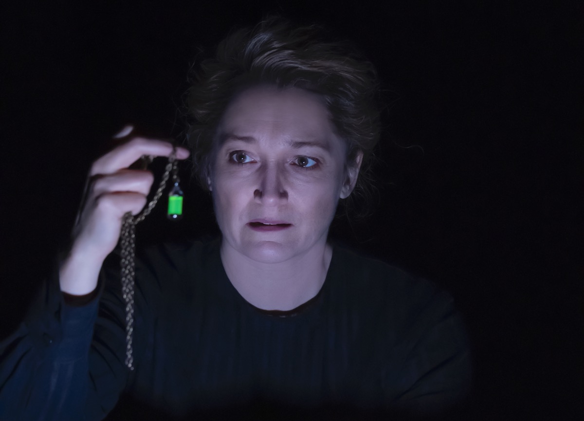 an actress playing marie curie holds a green glowing vial that represents radium