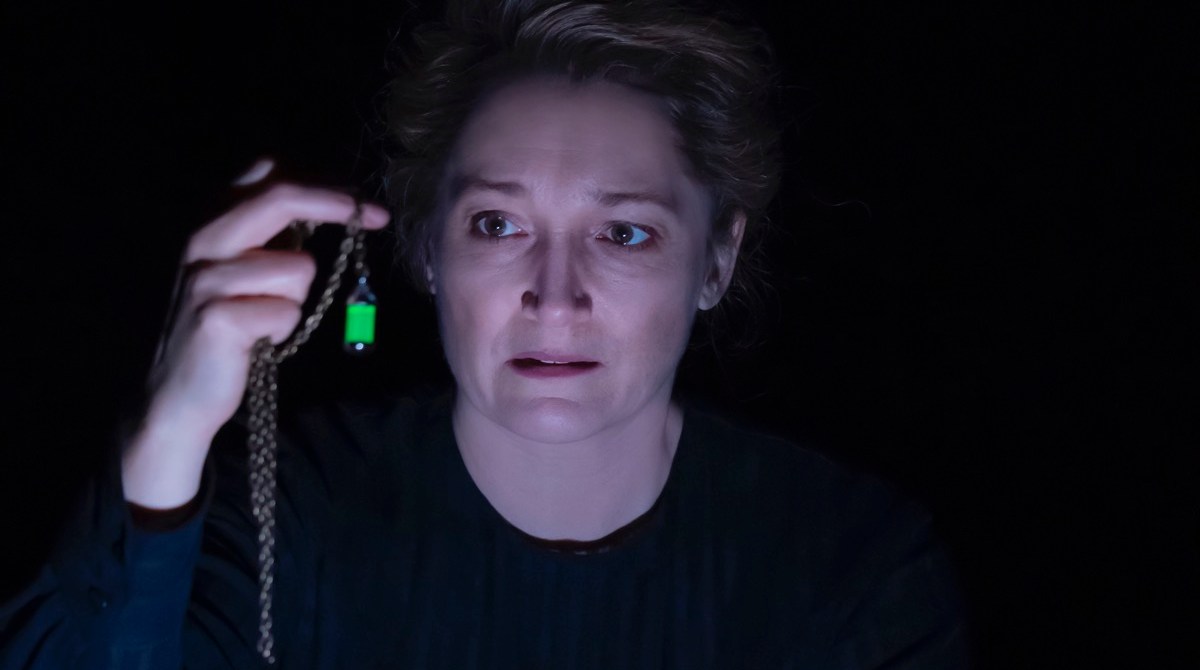 an actress playing marie curie holds a green glowing vial that represents radium