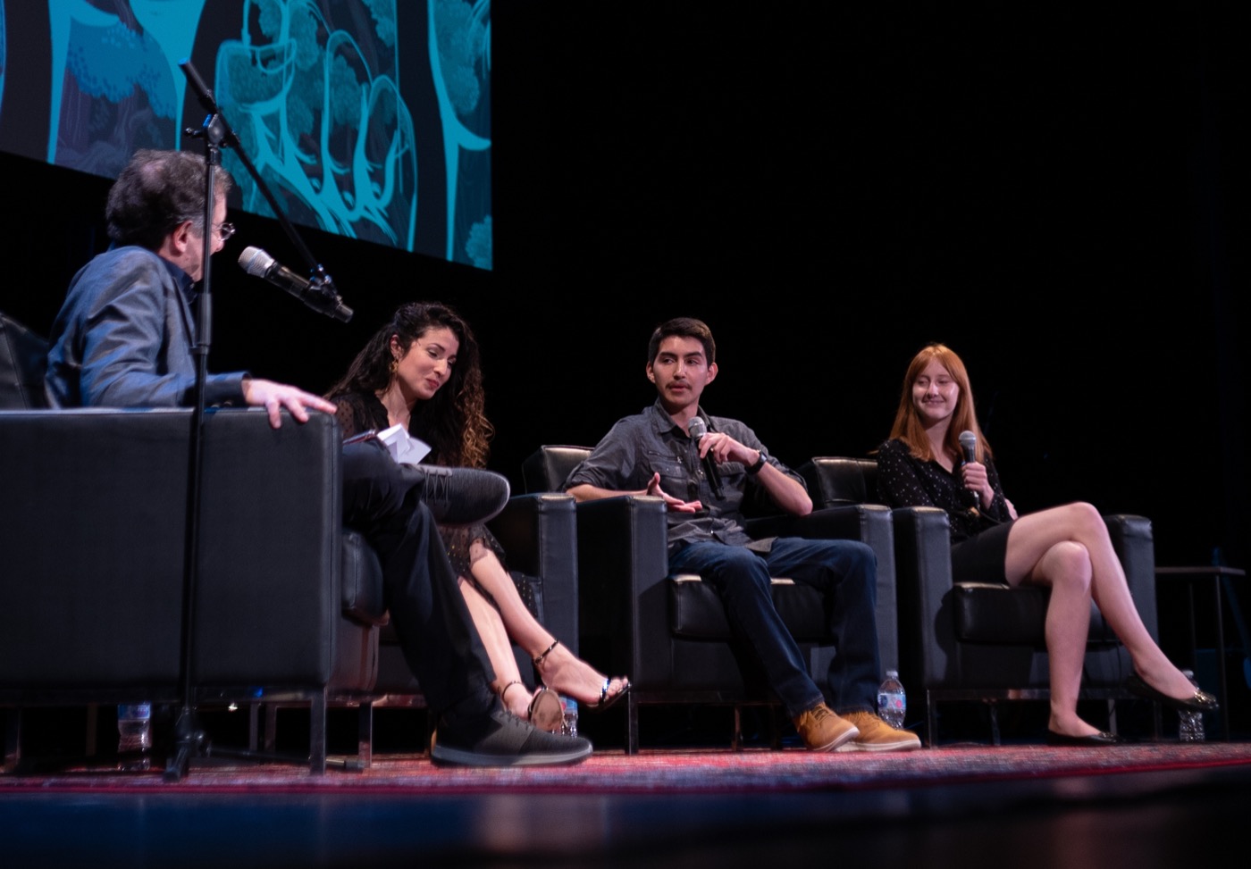 four people on chairs on a stage with mics