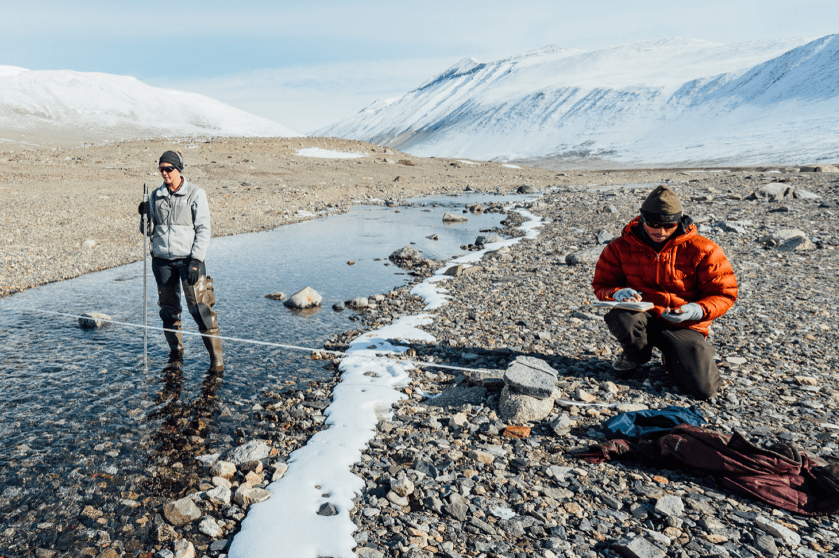 two researchers, one in a shallow river and the other on the side, taking measurements