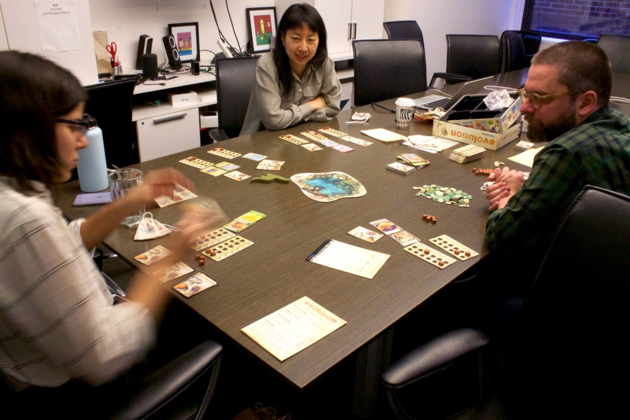 three people sitting at a table with cards playing a board game