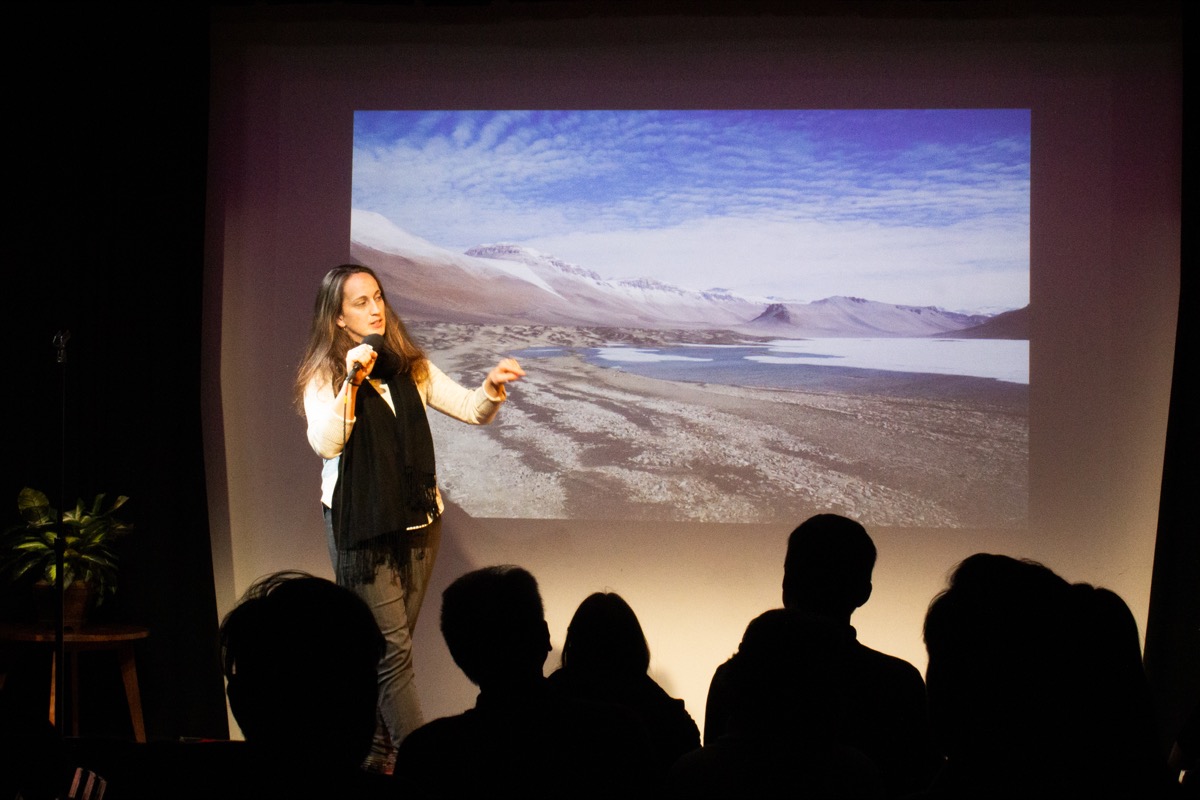 woman with a microphone on stage, with an image of an antarctic landscape behind her, in front of a seated crowd