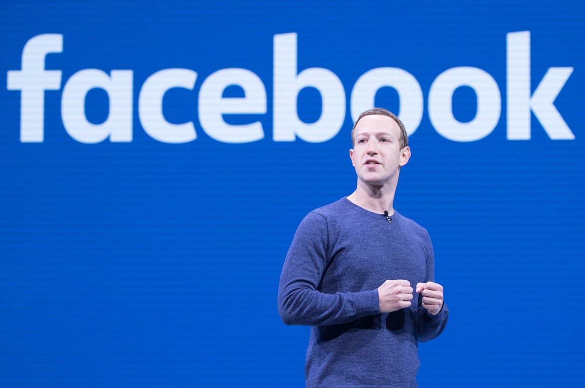 a man standing in front of blue screen with the facebook projected in white font