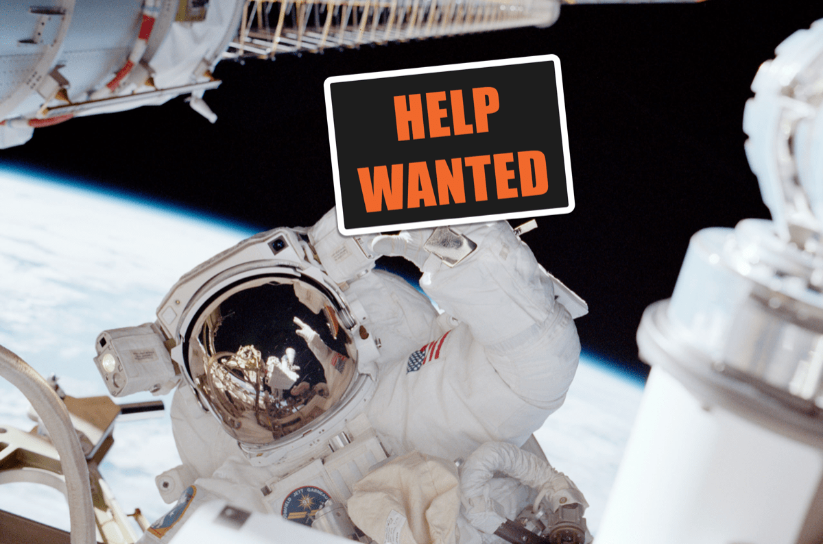 an astronaut in space on the international space station holds a photoshopped sign that says "help wanted"