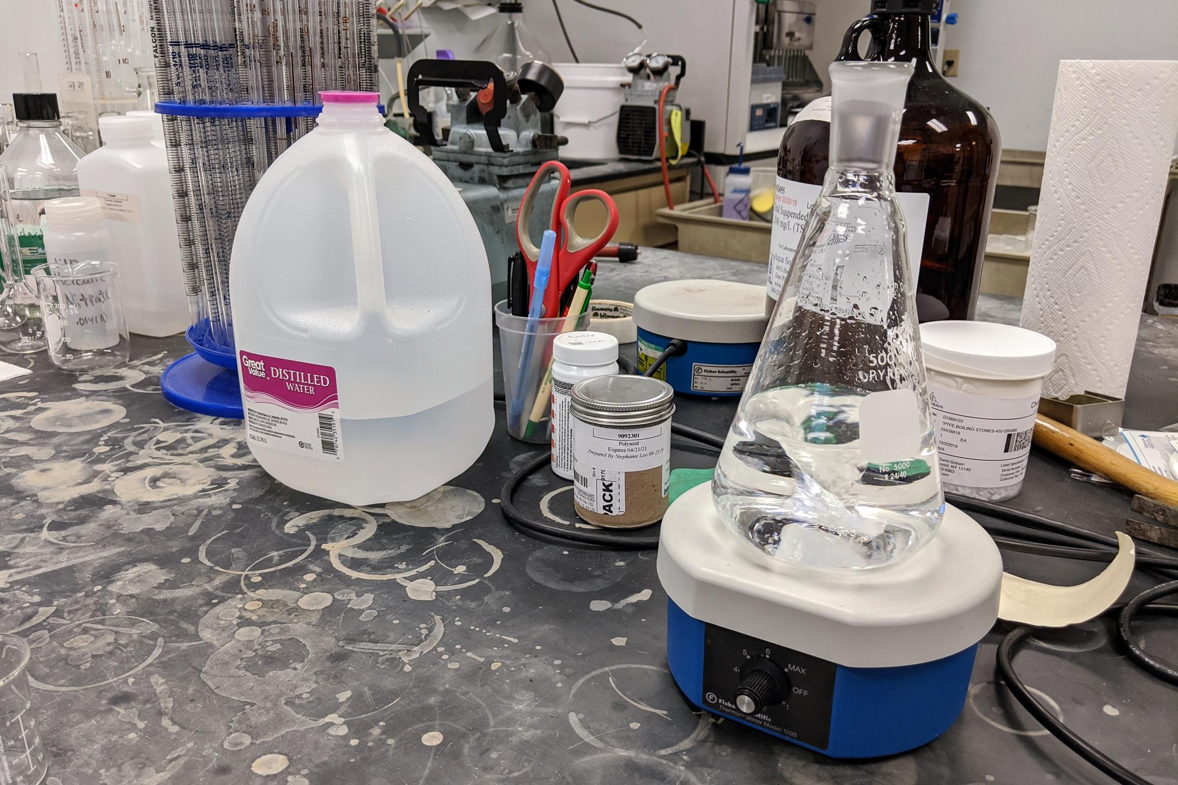 a table in a lab with a gallon jug of water and some beakers and testing equipment