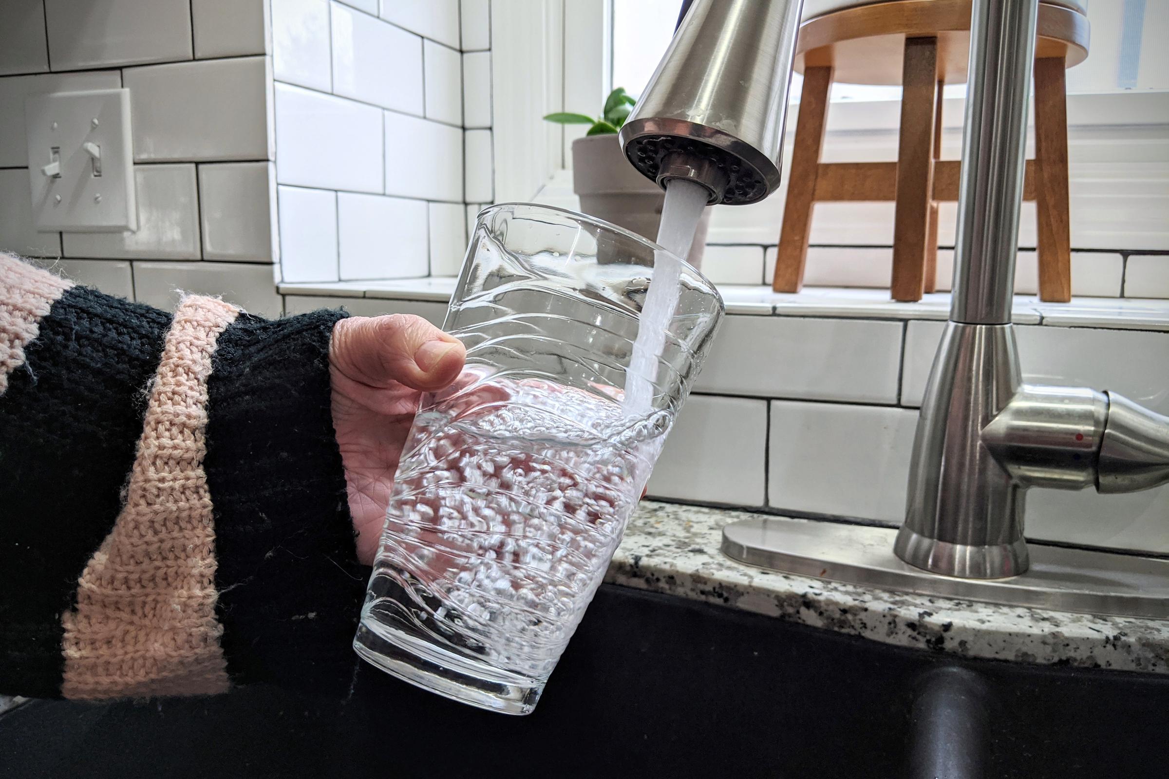 a person filling up a glass from water from the tap