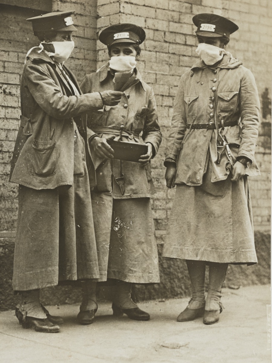 three women in conductor caps and coats wearing face masks