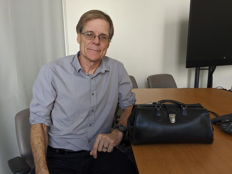 a man in glasses and a light blue button up shirt sits next to a table