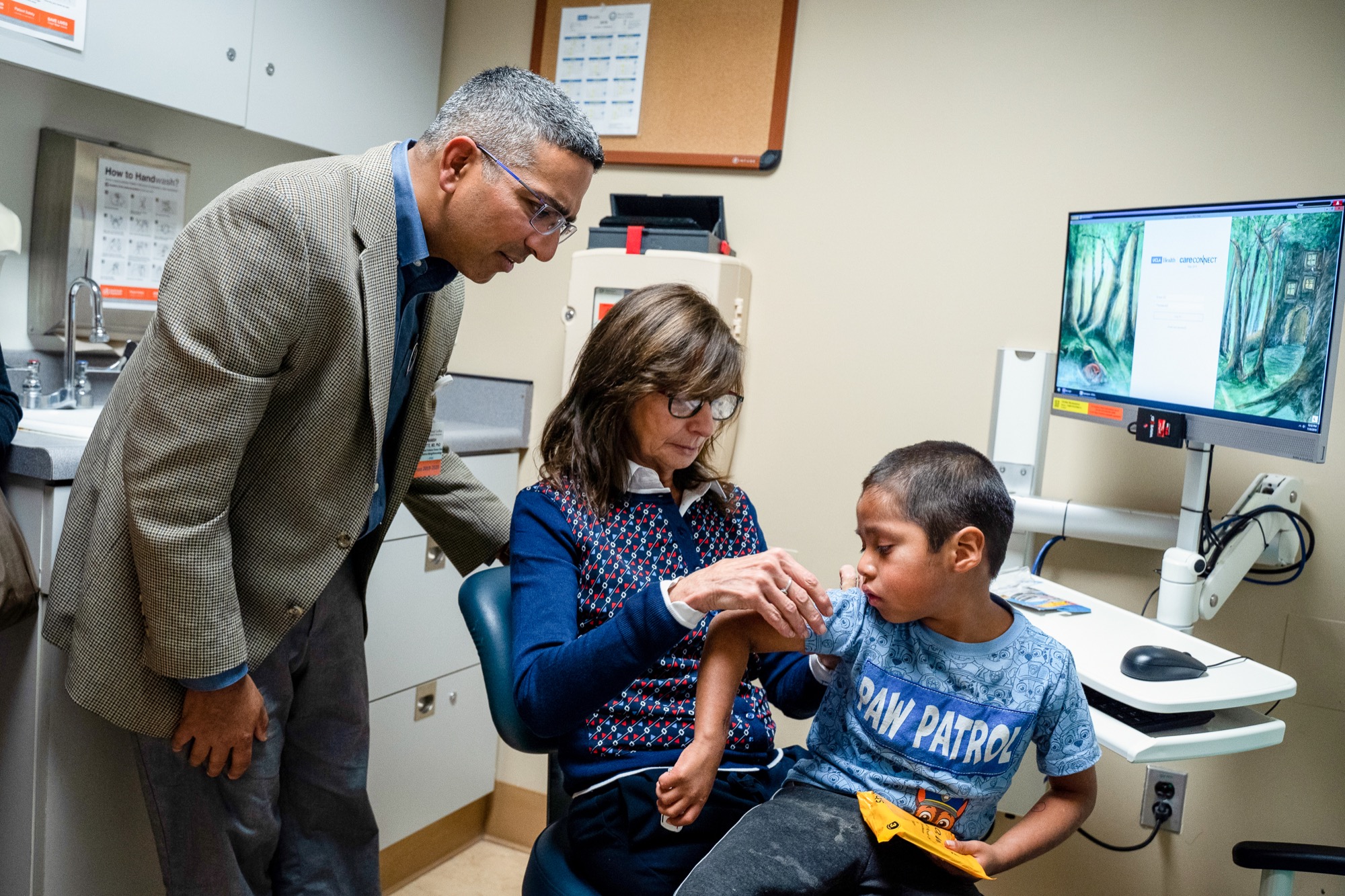 a young latino boy sits in a doctors office. a male and female doctor inspect a spot on his arm