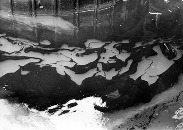 a black and white photo of dark patches of oil on a river
