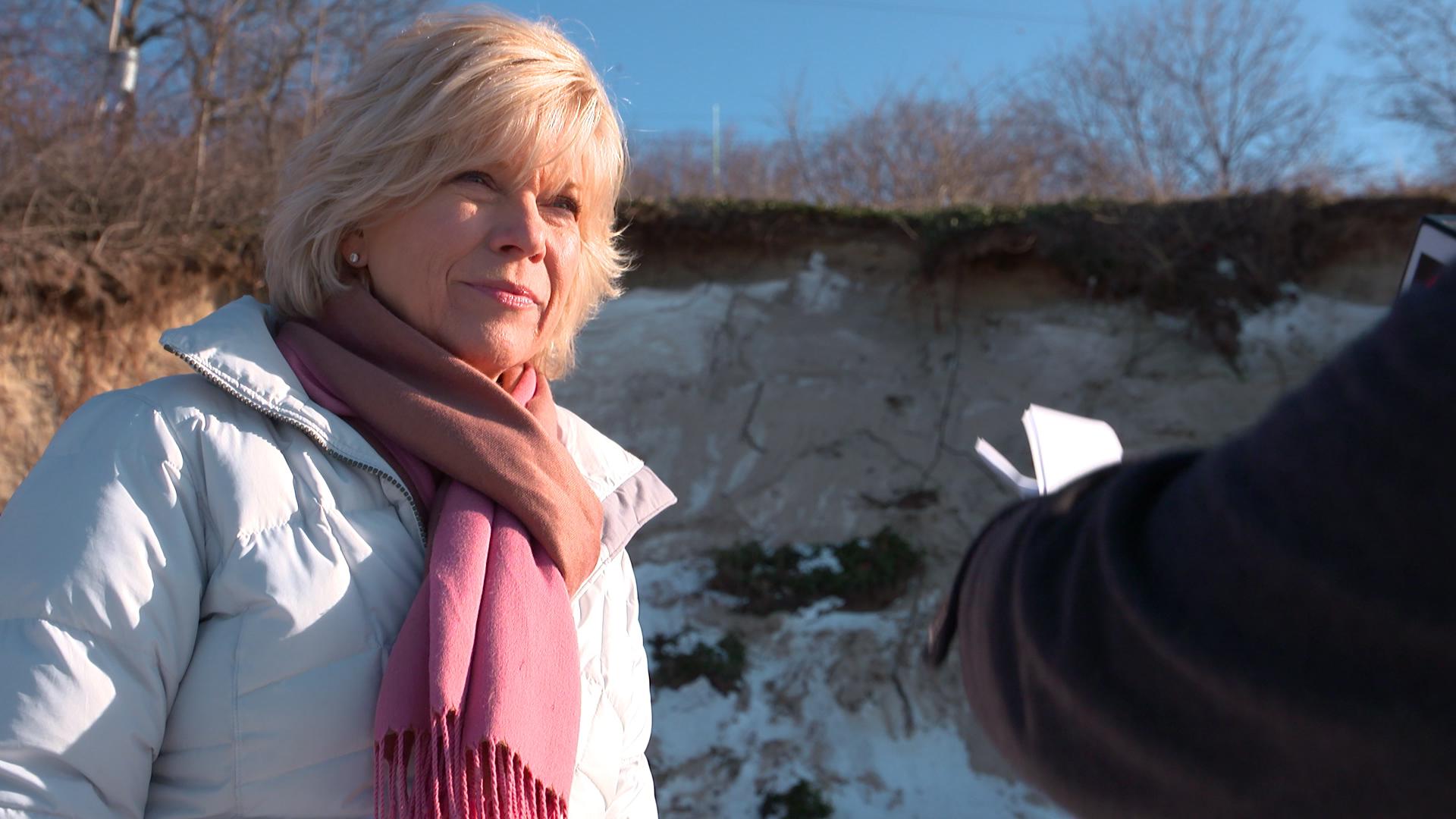 a woman with a scarf standing on a beach looking at someone