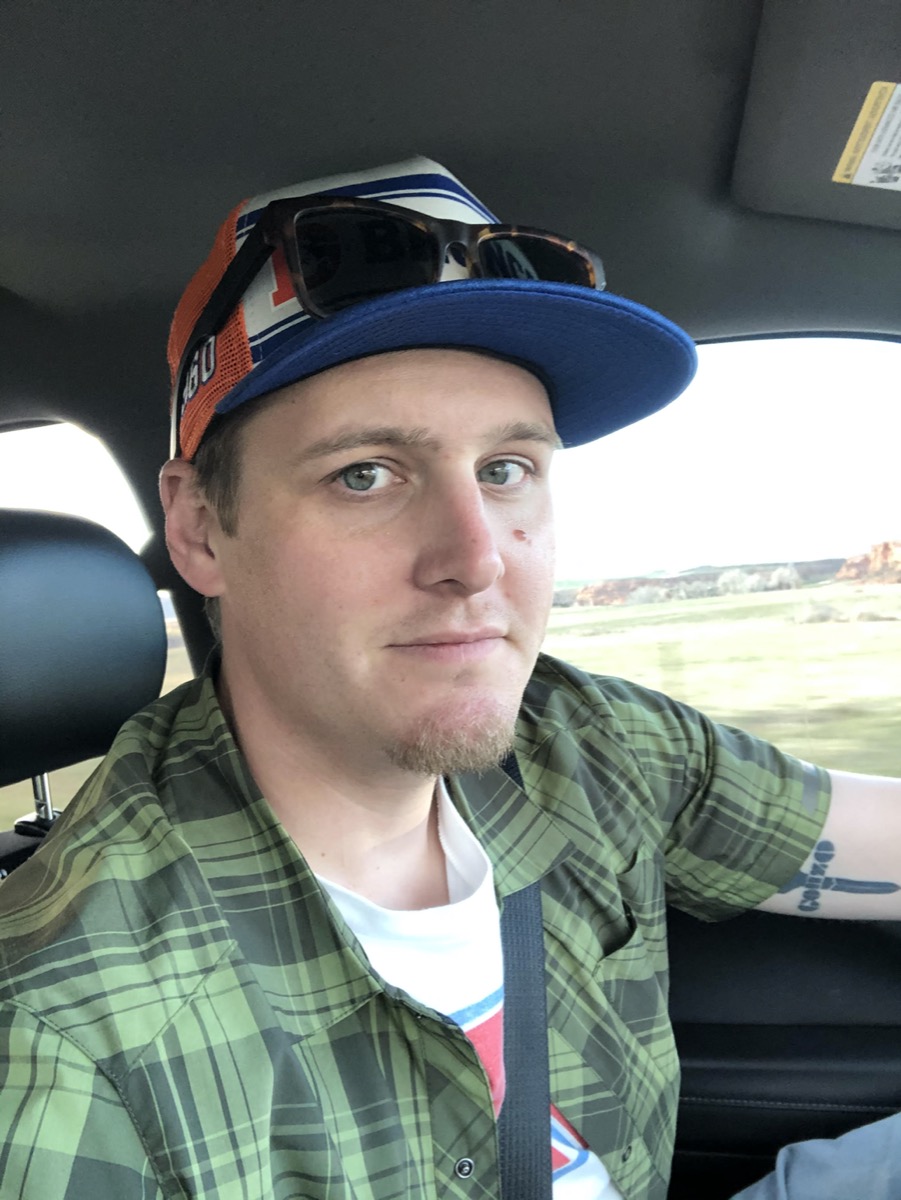 a young man in a green plaid shirt and sunglasses and hat